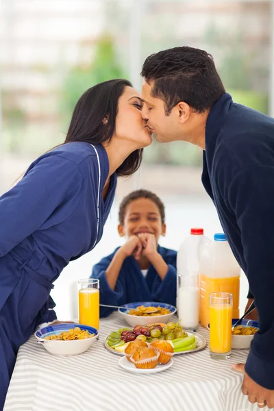 Menino está rindo ao ver os pais se beijando antes do café da manhã — Fotografia de Stock