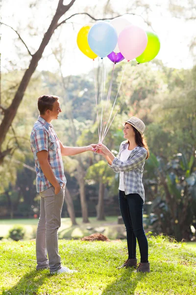 Teenage boy giving his girlfriend helium balloons — Stock Photo, Image