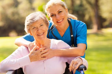 senior woman in wheelchair outdoors with caring caregiver