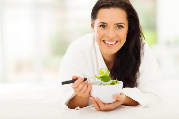 Donna sdraiata sul letto mangiare insalata di verdure — Foto Stock