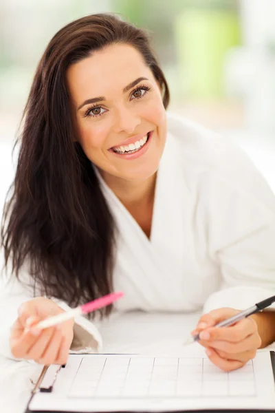 Mujer acostada en la cama escribiendo en un calendario — Foto de Stock