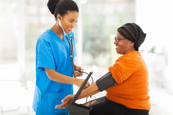 Afrikaanse verpleegster controle van senior patiënt bloeddruk — Stockfoto