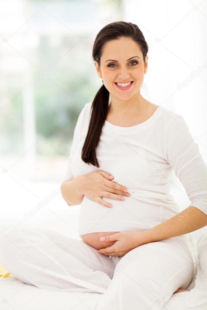 pregnant woman touching her belly while sitting on a bed