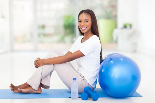 Mujer afroamericana sentada en la alfombra después de hacer ejercicio —  Fotos de Stock