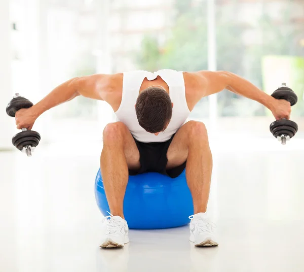 Hombre haciendo ejercicio con pesas sentado en la pelota de gimnasia —  Fotos de Stock