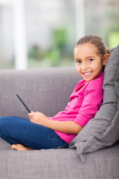 Niña sosteniendo la tableta del ordenador sentado en el sofá —  Fotos de Stock