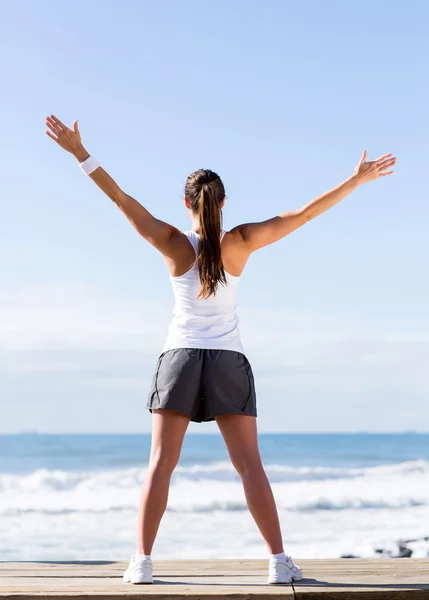 Bakifrån av kvinna stretching på stranden — Stockfoto