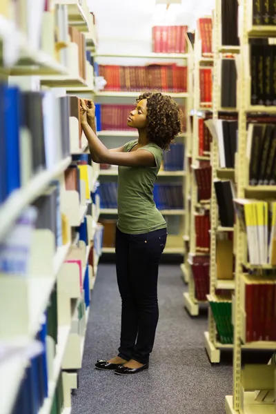 Gekrulde student op zoek naar een boek — Stockfoto