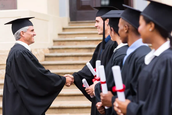 Absolventi v linii handshaking s děkanem — Stock fotografie