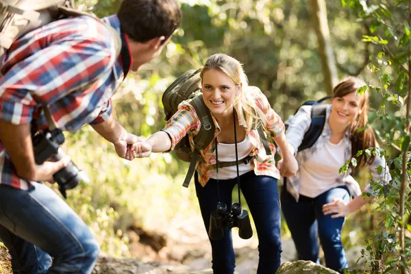 Young man helping friends to climb up — Stock Photo, Image