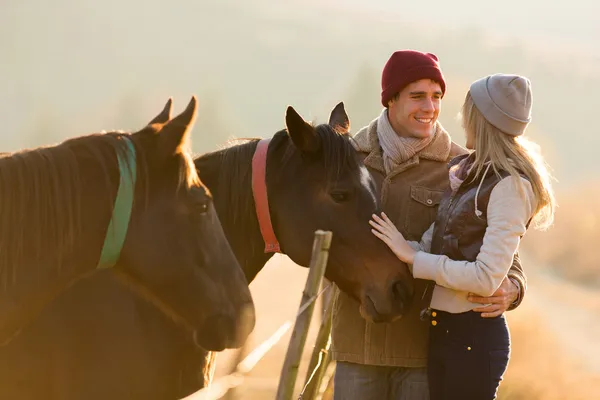 Junges Paar streichelt ein Pferd auf einer Koppel — Stockfoto