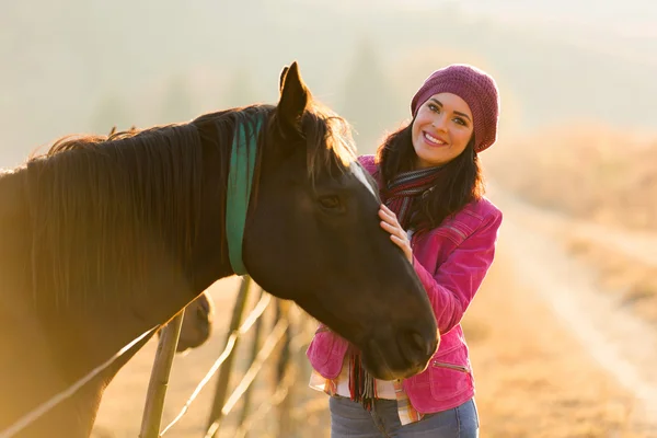 Joven mujer de pie junto a un caballo — Foto de Stock
