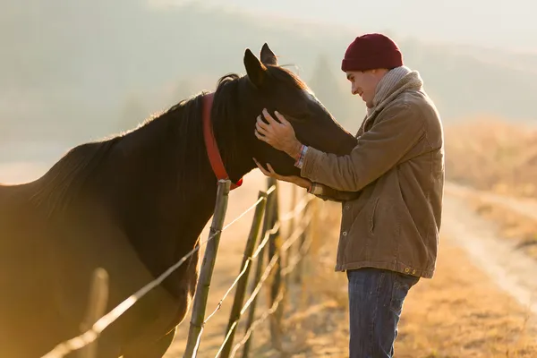 Giovane uomo che tocca il suo cavallo — Foto Stock
