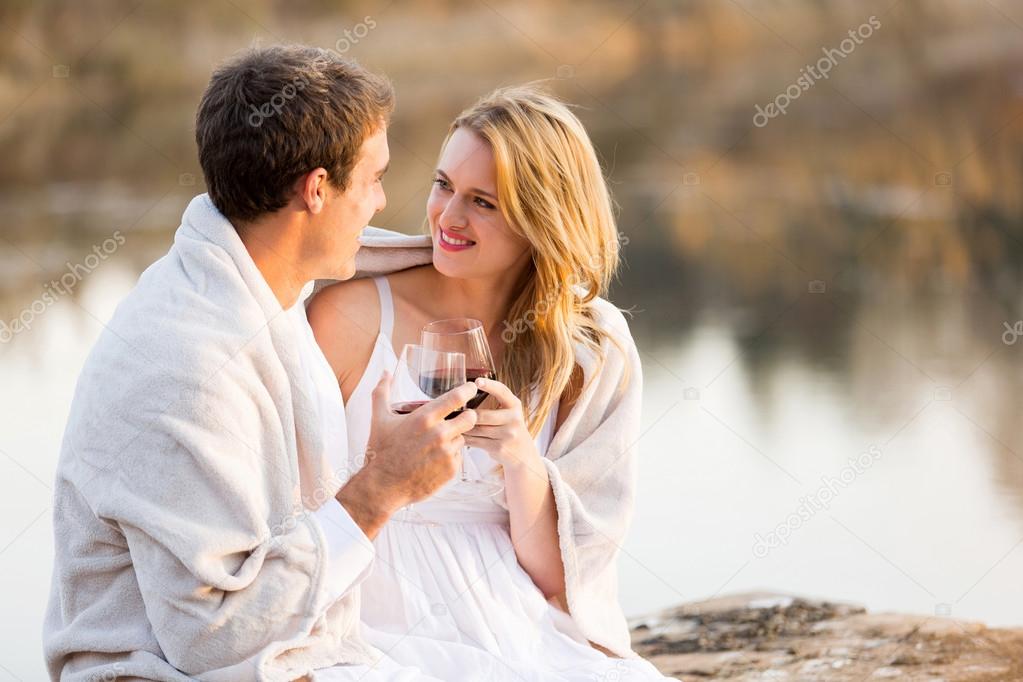 young couple sitting by a lake with wine