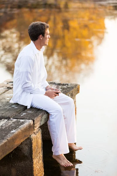 Jonge man zit op houten pier van het meer — Stockfoto