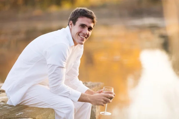 A fiatalember tárolás pohár bor mellett a tó — Stock Fotó