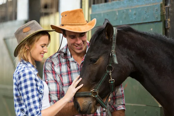 Cowboy e vaqueira confortando um cavalo no estábulo — Fotografia de Stock