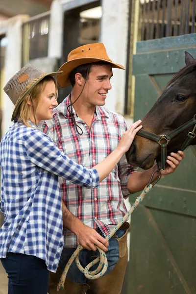 Kowboj i cowgirl w stajni dotykając konia — Zdjęcie stockowe