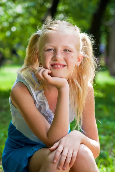 Sweet, playful blond girl sitting in the green garden and backin — Stock Photo, Image