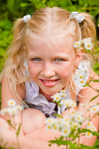 Blonde girl, her freckled face, sitting in the green grass with — Stock Photo, Image