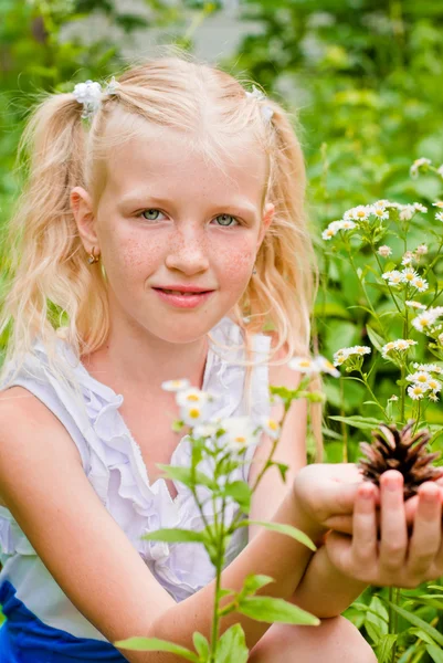 Blonde girl with two tails, sitting in the green grass with flow — Stock Photo, Image