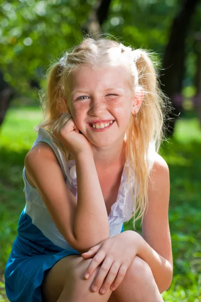 Sweet, playful blond girl sitting in the green garden and backin Royalty Free Stock Photos