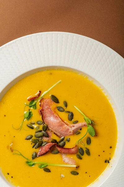 Bezelye tohumlu pastırmalı balkabağı çorbası ve güzel beyaz bir tabakta filizler. Basit, sağlıklı besleyici yiyecekler. Ev yapımı yemekler bir restoranda servis edilir.