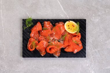 Baharatlı siyah bir tabakta dilimlenmiş tuzlu somon. Kırmızı et balığı, besleyici atıştırmalık, omega, baharatlı balık ve dereotlu restoran.