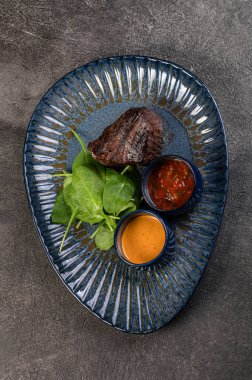Ispanaklı ızgarada ızgara biftek ve parlak mavi bir tabakta sos. Yürekli bir gurme yemeği. Basit geleneksel yemek, öğle yemeği fikri. Restoran malzemeleri..