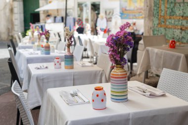 Bir kafede iyi servis edilen masalar, vazolarda taze renkli çiçekler, beyaz masa örtüleri, yaz terası. İtalya 'da tatiller, Amalfi. Kolay servis