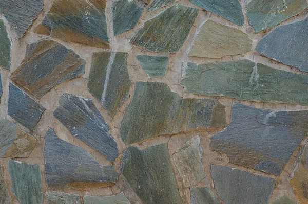 The wall is made of pieces of colored stone - blue, brown, gray. Hand masonry. Texture, background