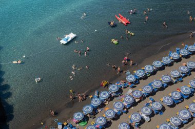 Manzara - Sorrento 'daki Tyrhenian Denizi' nde güneşli yataklı ve şemsiyeli tatilciler için bir plaj. Napolitan Körfezi 'nde sıcak yaz, İtalya' da Avrupa tatili