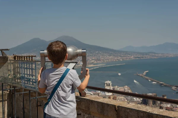 Children\'s tourism in Europe. Little boy with binoculars looking at the city of Naples, Italy. It looks at the mountains and Vesuvius. Education of children through recreation. Interest and interest