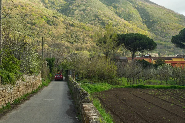 Country road with a red car leading to an old forgotten ruined villa in the mountains of southern Italy. Peaceful village life, retro recreation in nature. European weekend (holiday)