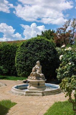 Garden sculpture - a dried (neglected) fountain with a beautiful woman and child on the paths of a green summer garden in Italy