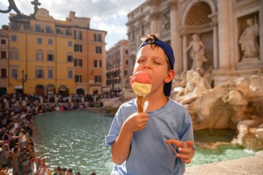 Cute cheerful boy 7 years old eating ice cream (gelato) near the Trevi Fountain in Rome, Italy. Traveling with children, family vacation, intellectual development of the child