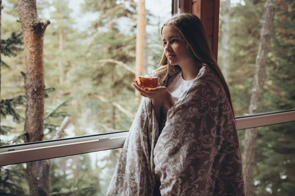 Дівчина п'є чай на природі. Красива молода дівчина стоїть біля вікна і тримає чашку чаю в руках . — стокове фото