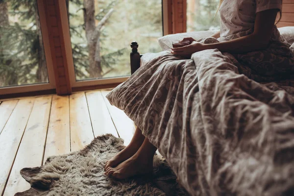 La fille boit du thé dans la nature. Une belle jeune fille se tient à la fenêtre et tient une tasse de thé dans ses mains. — Photo