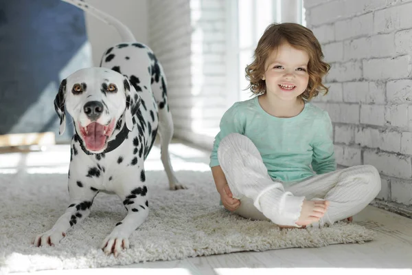 Un niño con un perro. Una chica feliz yace en una alfombra con un perro dálmata. — Foto de Stock
