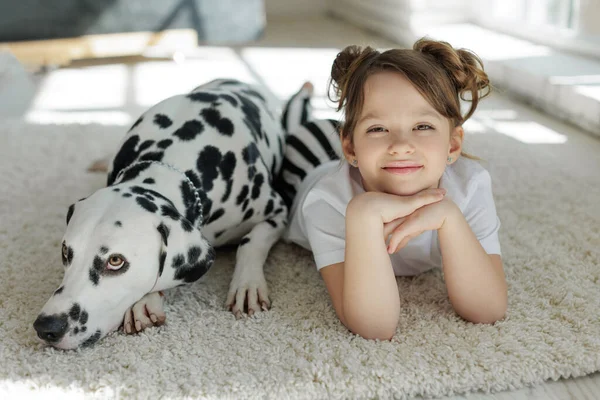 Un niño con un perro. Una chica feliz yace en una alfombra con un perro dálmata. — Foto de Stock