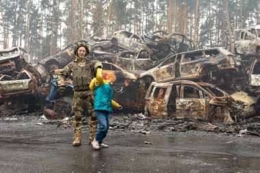 IRPIN, Kyiv bölgesi Ukrayna - 22.04.2022: araba mezarlığı. Askeri kadın, çocuğun tahliye edilmesine yardım ediyor. Rusya 'nın Ukrayna' ya karşı savaşı
