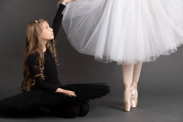 小女孩穿着芭蕾舞鞋坐在芭蕾舞演员的腿旁边 图库照片