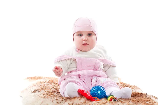 Little girl sitting on a fur rug with toys — Stock Photo, Image