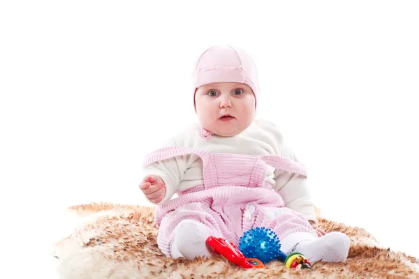 Menina sentada em um tapete de pele com brinquedos — Fotografia de Stock