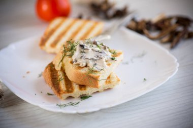 Kızarmış ekmek tostu, peynirli, haşlanmış mantarlı, ahşap bir masada..