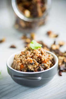 Sebzeli haşlanmış karabuğday ve ahşap bir masada seramik bir kalıpta kurutulmuş orman mantarı.