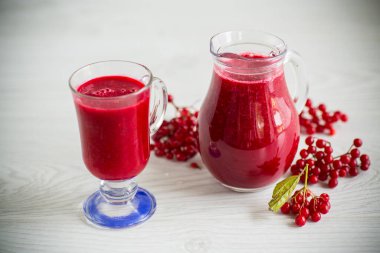 Taze sıkılmış, olgun kırmızı viburnum hamuruyla ahşap bir masada bir sürahide taze sıkılmış doğal meyve suyu.