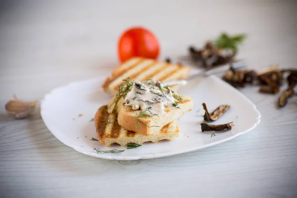 Gebratenes Brot Toast mit Käseaufstrich mit gekochten getrockneten Pilzen auf einem Holztisch. — Stockfoto