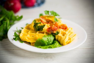 Domatesle doldurulmuş yumurta omleti ve waffle şeklinde kızarmış sebzeler, ahşap bir masada..