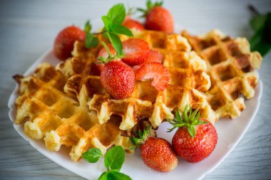 Tahta bir masanın üzerinde taze çilekle pişirilmiş tatlı kremalı waffle..